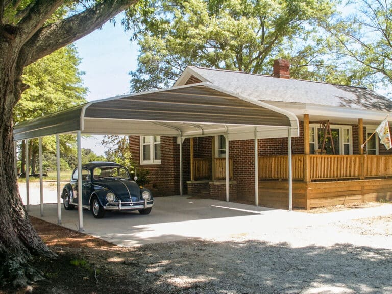 Carports for sale in Abbeville, SC: A metal carport with a curved roof, providing shade for a classic car, situated in front of a charming brick house with a wooden porch and surrounded by trees